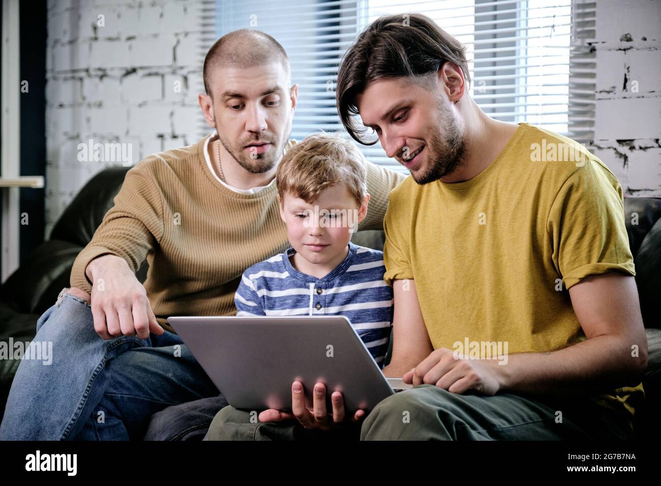 Two fathers and their preteen son spending time together at home and watching movie or playing game on laptop Stock Photo