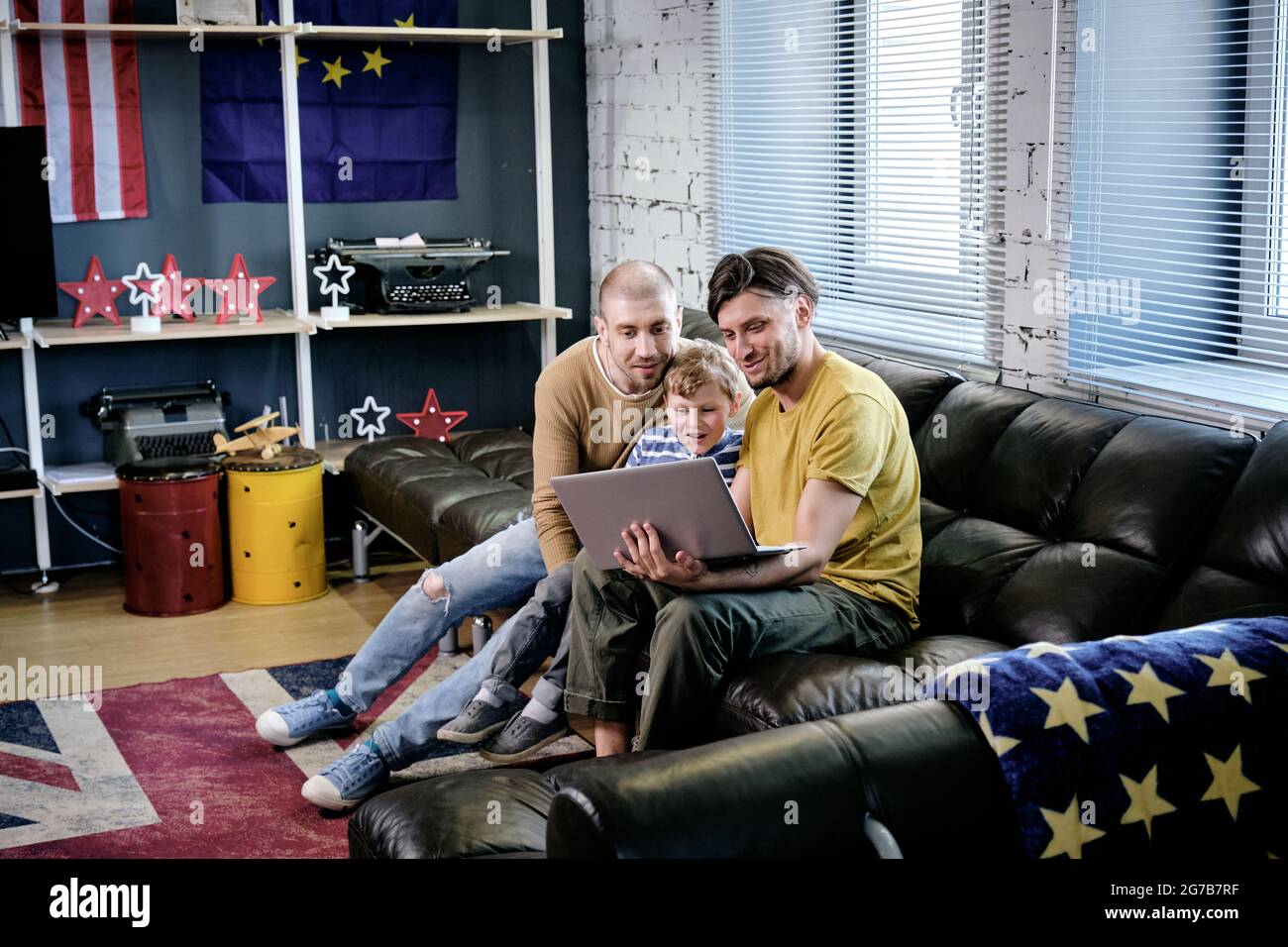 Excited little boy and his two fathers watching interesting movie or animated cartoon on laptop when spending weekend at home Stock Photo