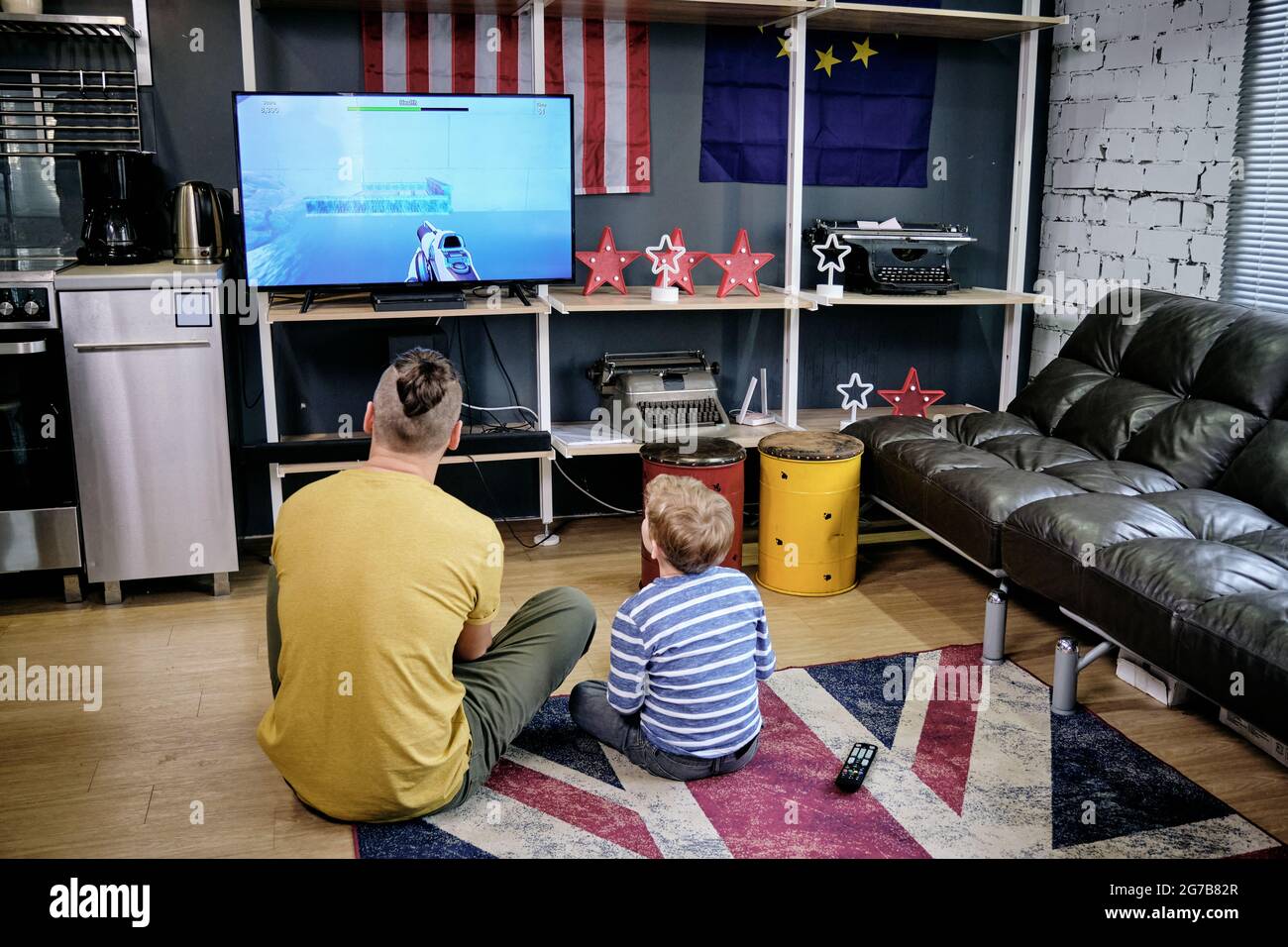 Back view of young man and little boy playing video game on the floor at home Stock Photo