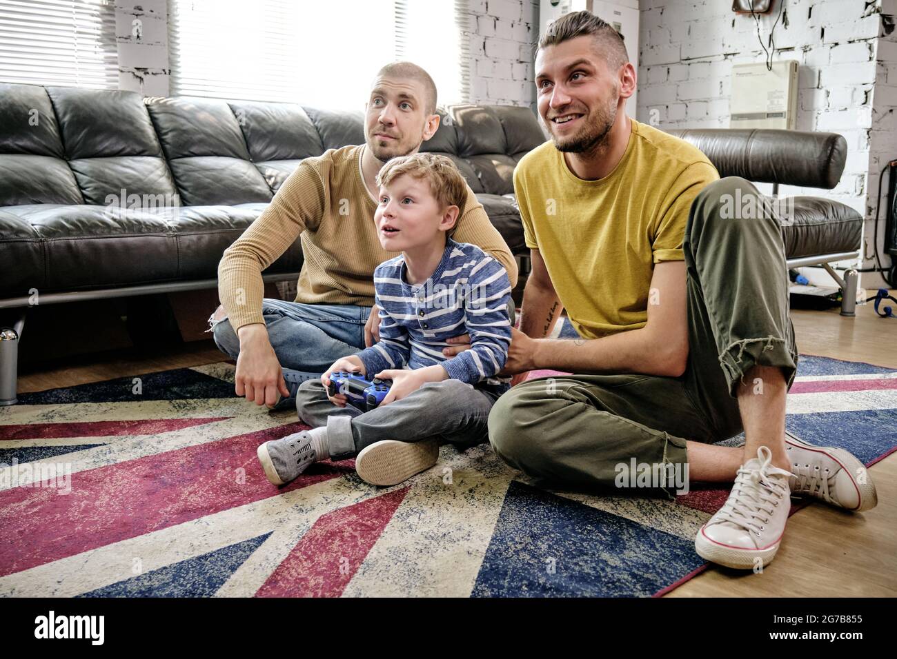 Two happy fathers supporting their little son playing videogame on console Stock Photo
