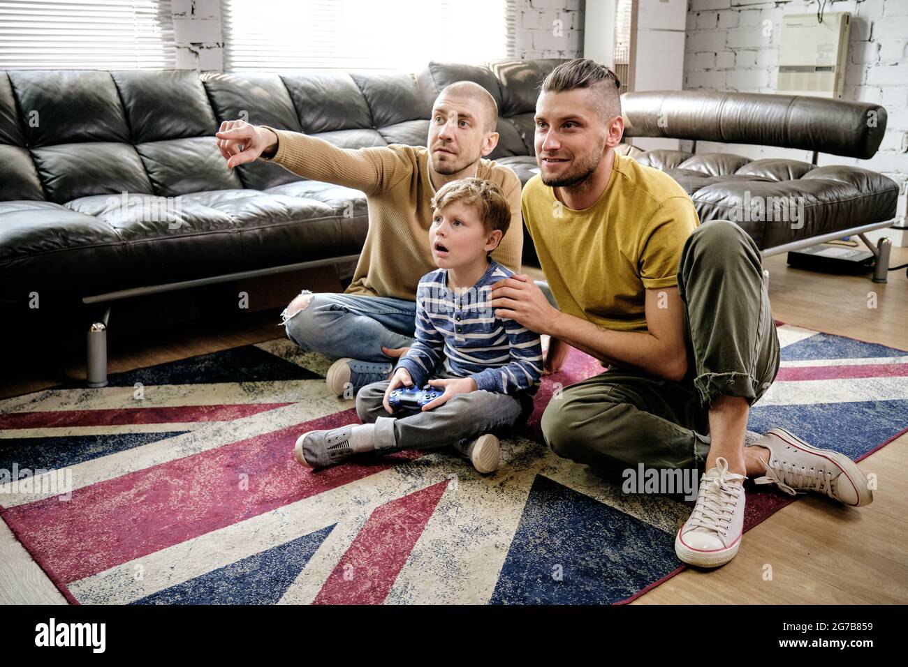 Amazed preteen boy and two guys sitting on the floor and playing new videogame at home Stock Photo