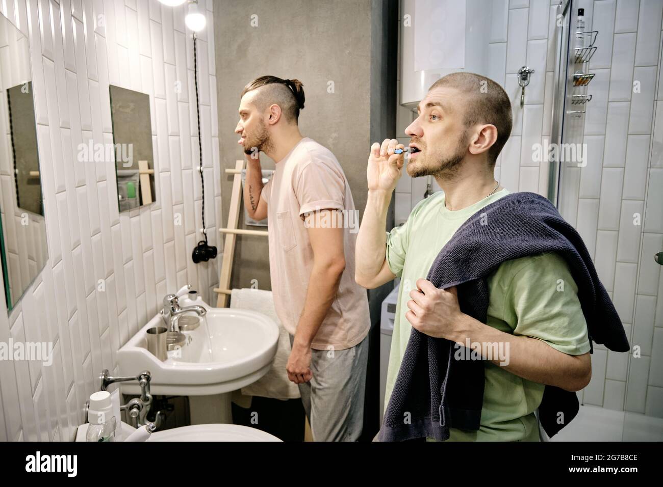 Young men brushing teeth in front of mirrors in dorm bathroom in the morning Stock Photo