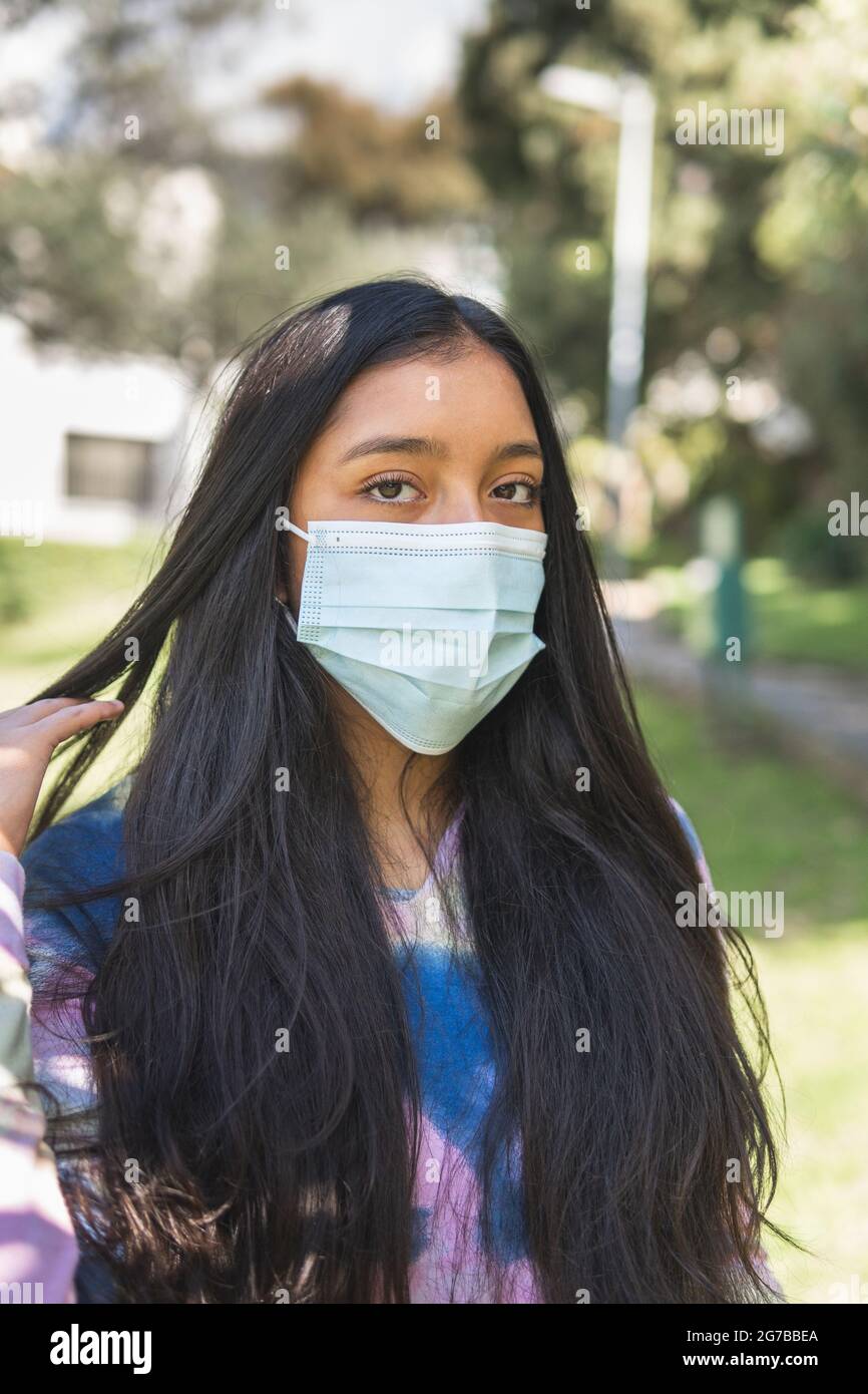 Close-up of a Latina teen girl wearing a mask combing her hair with her ...