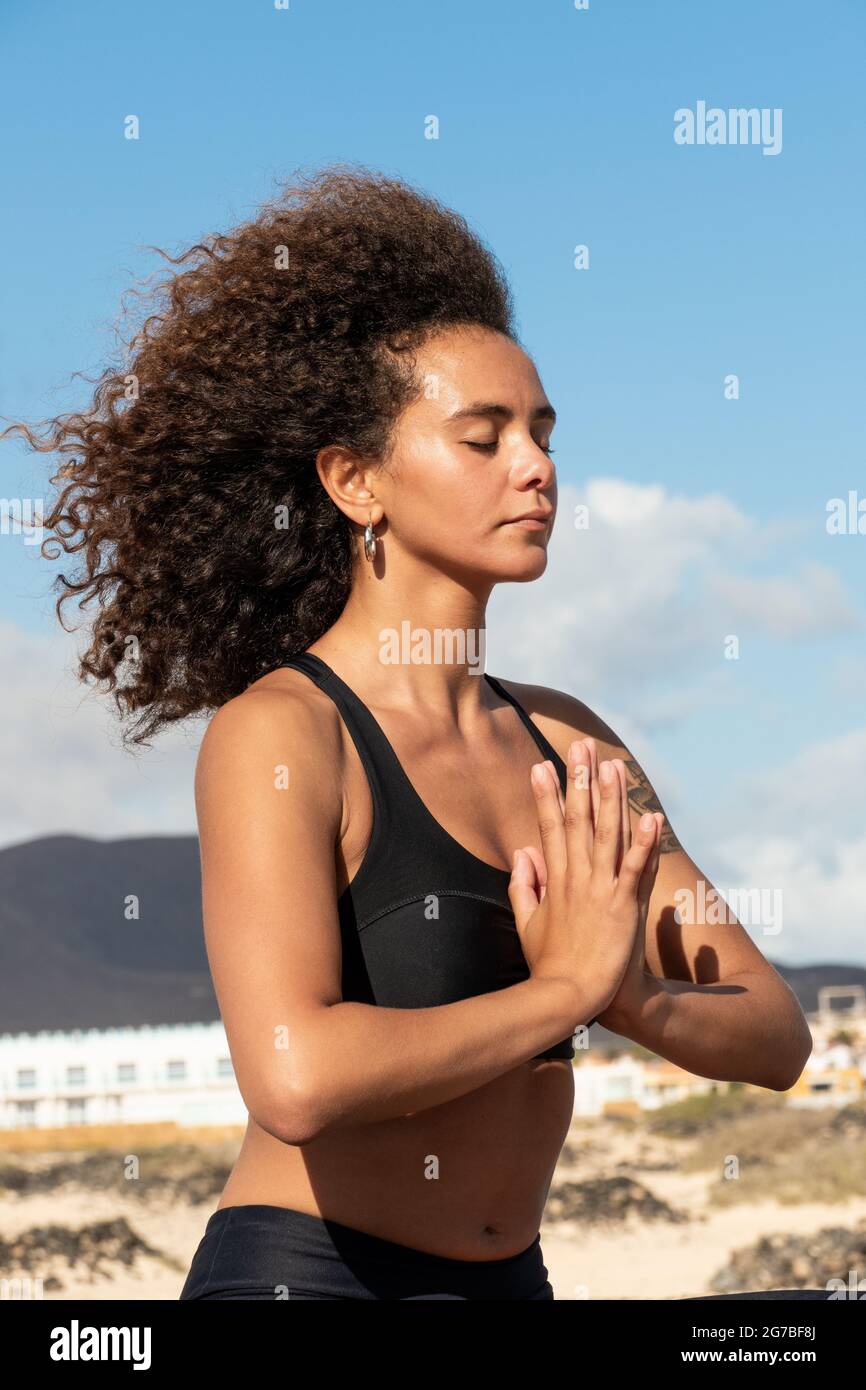 Afro young woman portrait sitting outdoors on yoga position with hands together Stock Photo