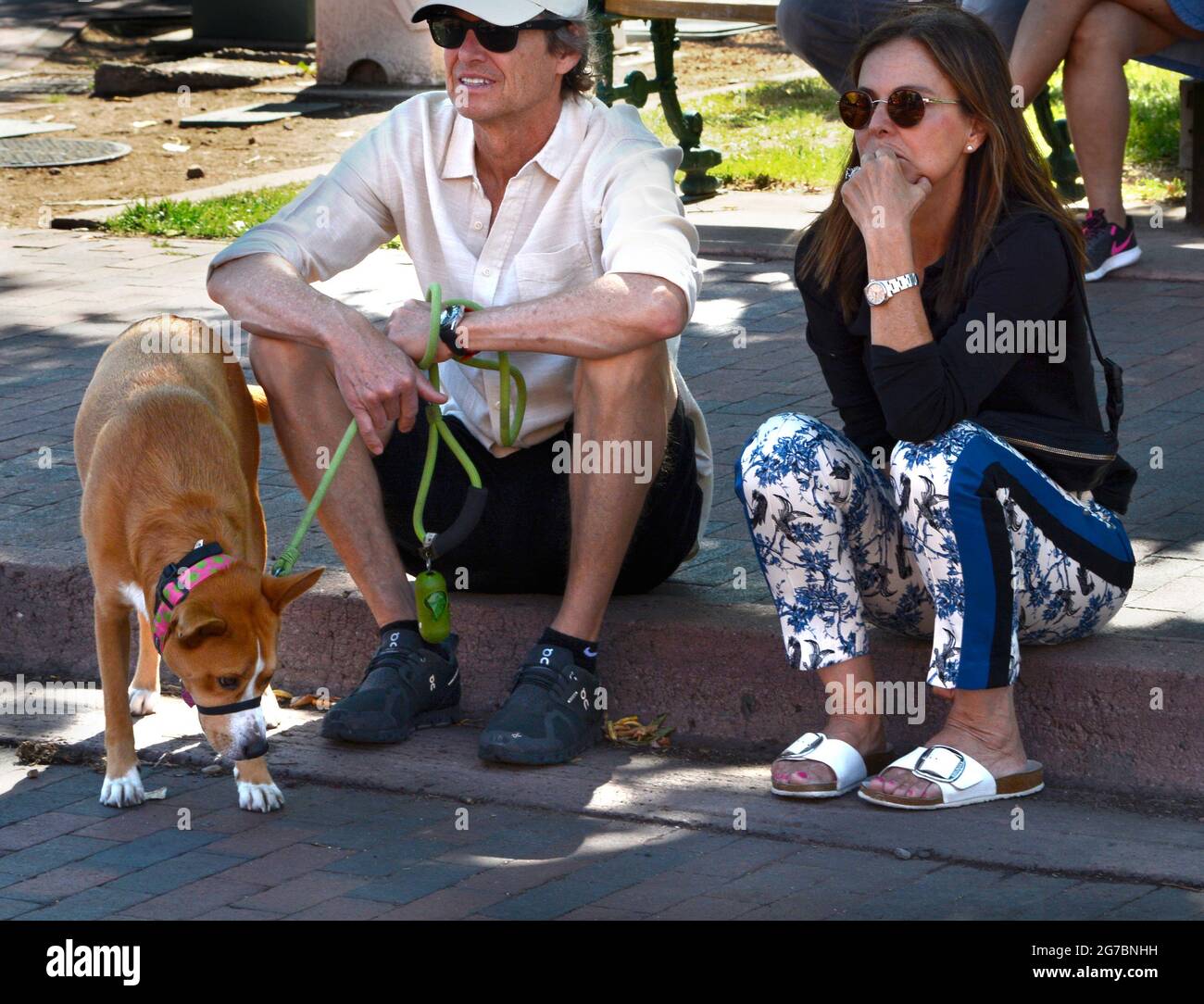 A couple vacationing in Santa Fe, New Mexico, sit on a curb with their dog and people-watch. Stock Photo