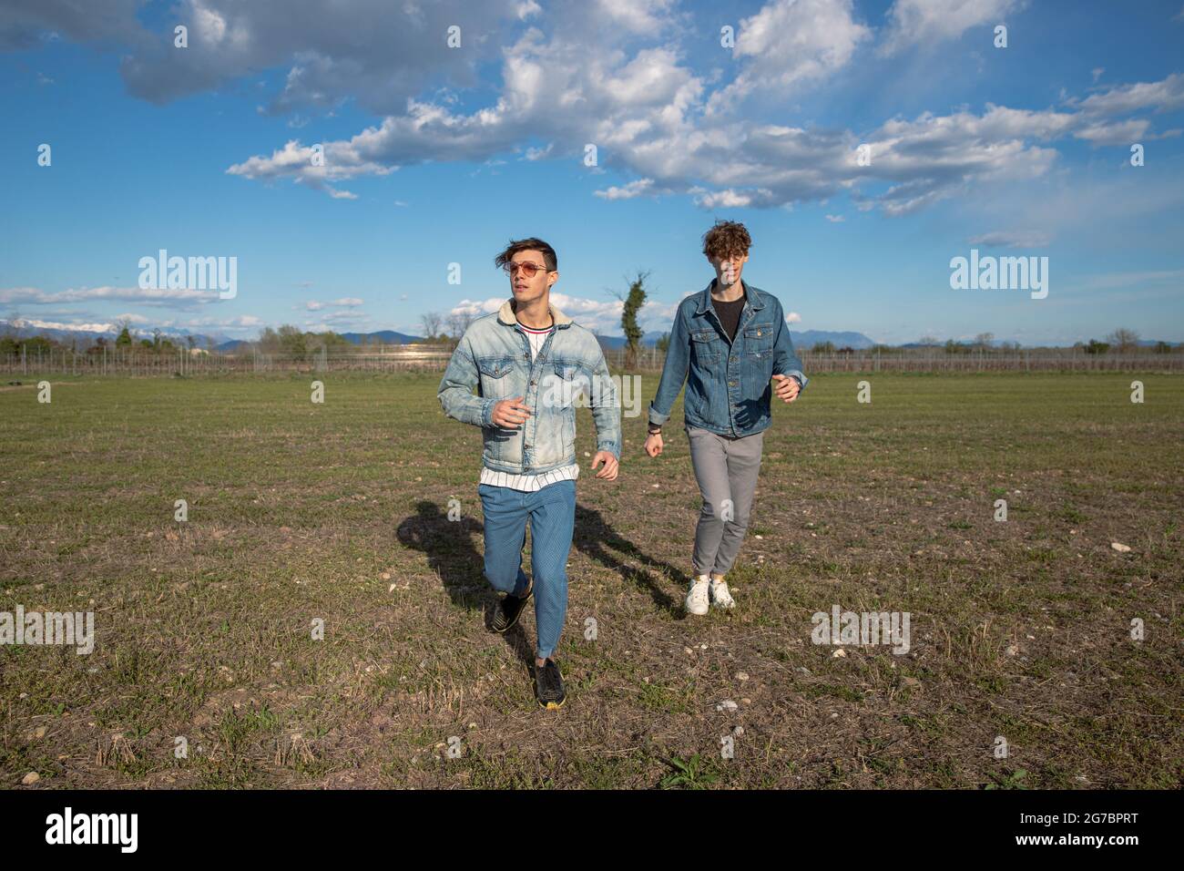 Two brothers run in a field of grass in the open air, young men dressed causally, wearing denim jackets. brotherhood concept. Stock Photo