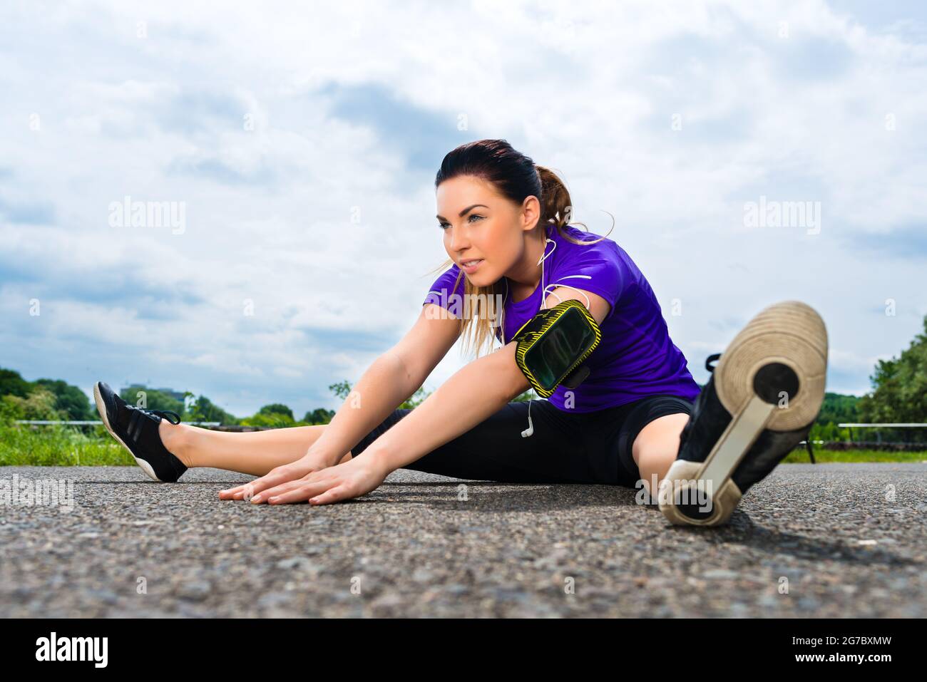 Urban sports - young woman is doing warming up before running in the greenfield on a summer day Stock Photo