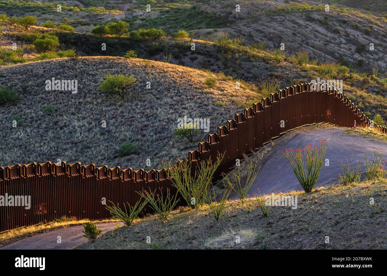 US border fence on the Mexico border, east of Nogales Arizona and Nogales Sonora Mexico, viewed from US side at sunset, looking southwest.This type of Stock Photo