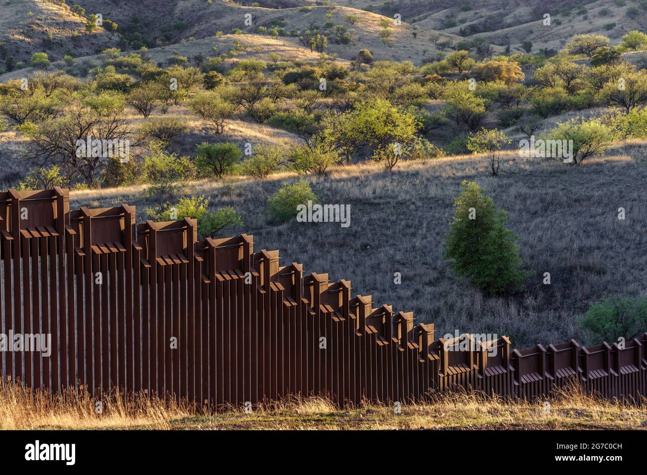 Image shows US border fence on the Mexico border, east of Nogales Arizona and Nogales Sonora Mexico, viewed from US side with typical vegetation domin Stock Photo