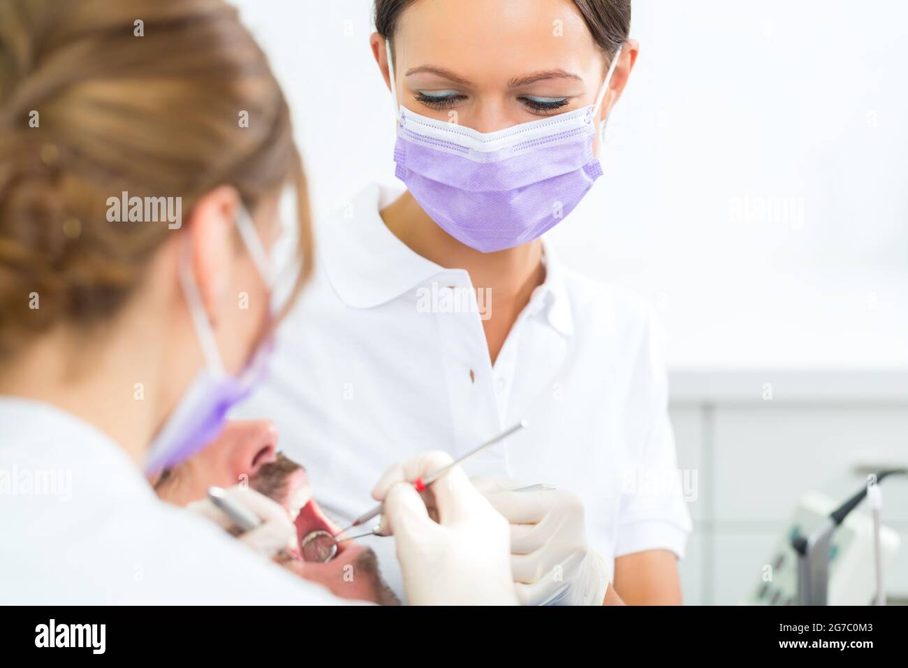 dentist in her practice or office treating male patient with assistant