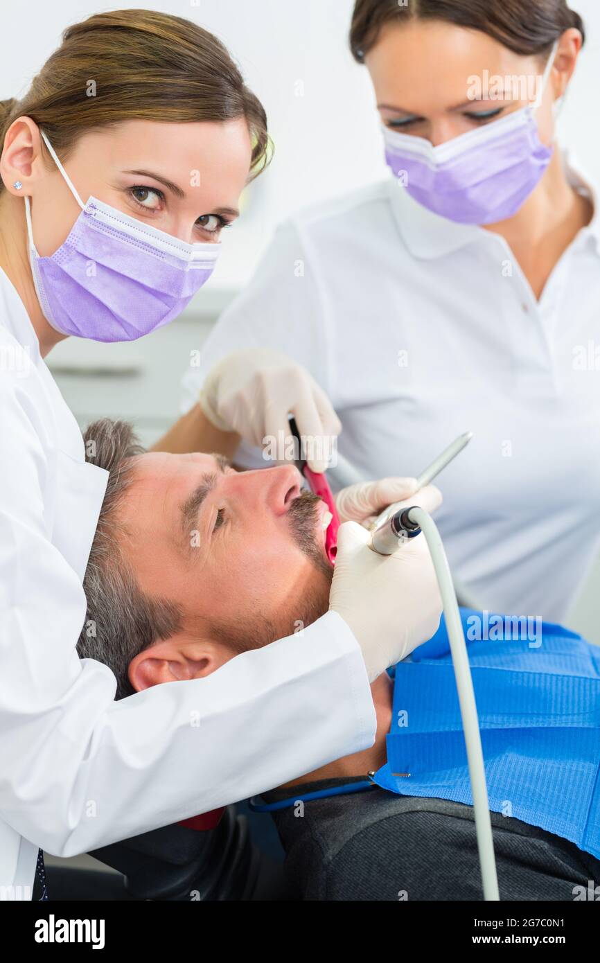 dentist in her practice or office treating male patient with assistant