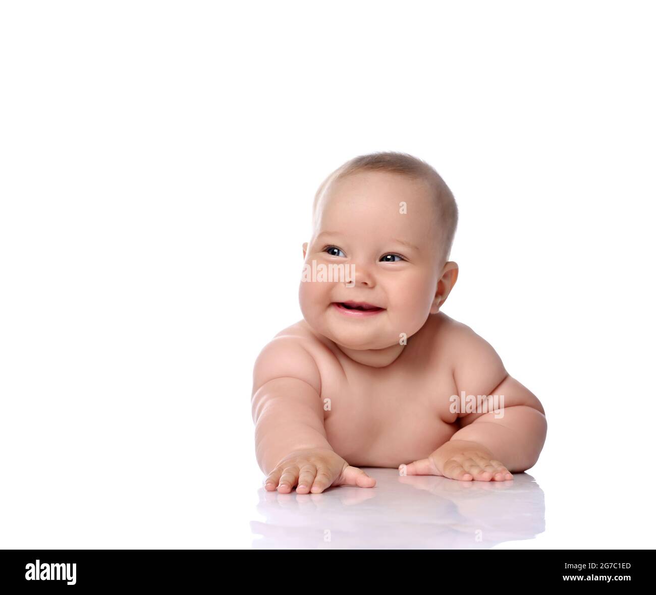 Happy laughing infant child baby girl kid in diaper is lying on her tummy holding arm outstretched, slapping on floor  Stock Photo