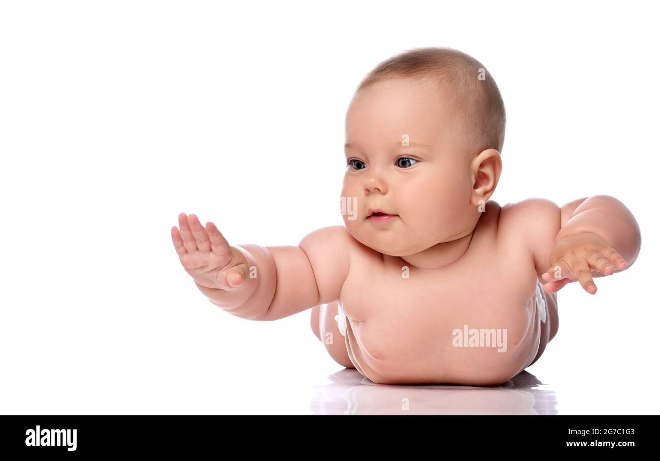 Infant child baby girl kid in diaper is lying on her tummy, stomach holding hands up, slapping on floor  Stock Photo