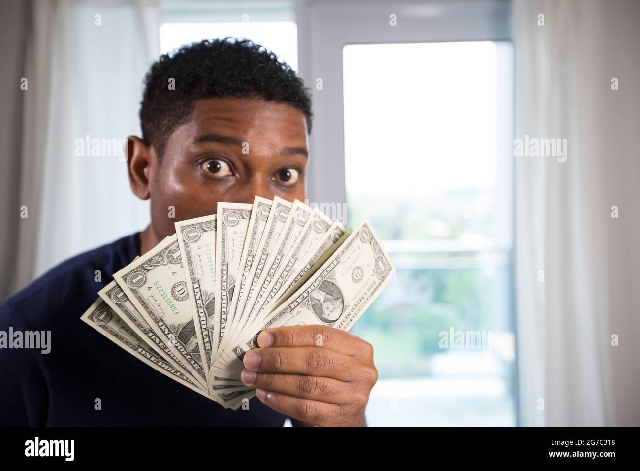 African American man holds up us currency to his face with eyes wide open, camera focuses on the money. Stock Photo