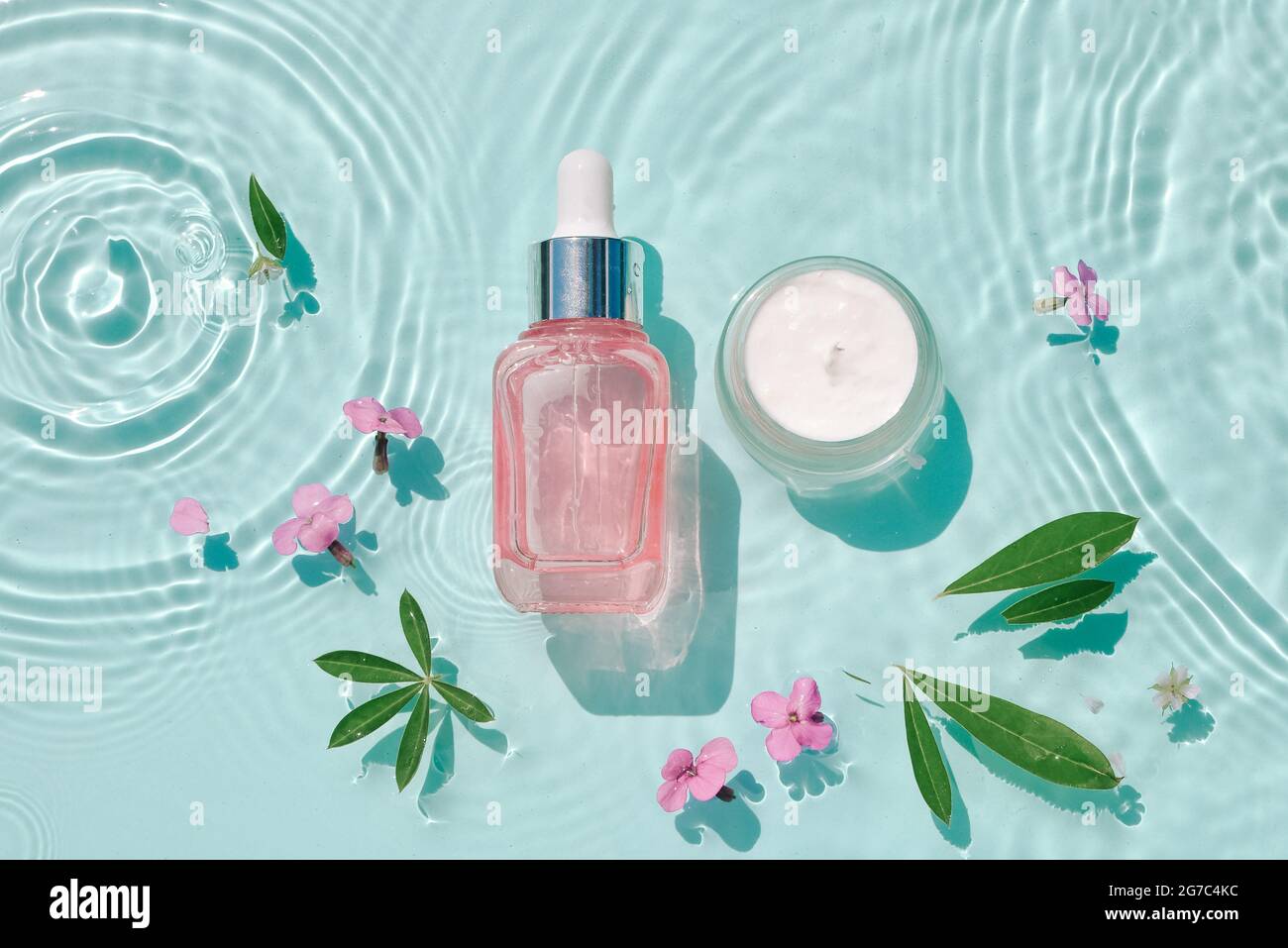 Set moisturizing cosmetic products on water with drops. Serum glass bottle and cream jar on aqua surface with waves in sunlight. Concept for advertisi Stock Photo