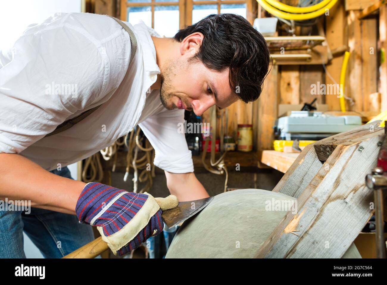 Young man in the Bavarian mountains grinds his axe and sharpening tools with a grindstone to chop the fire wood Stock Photo