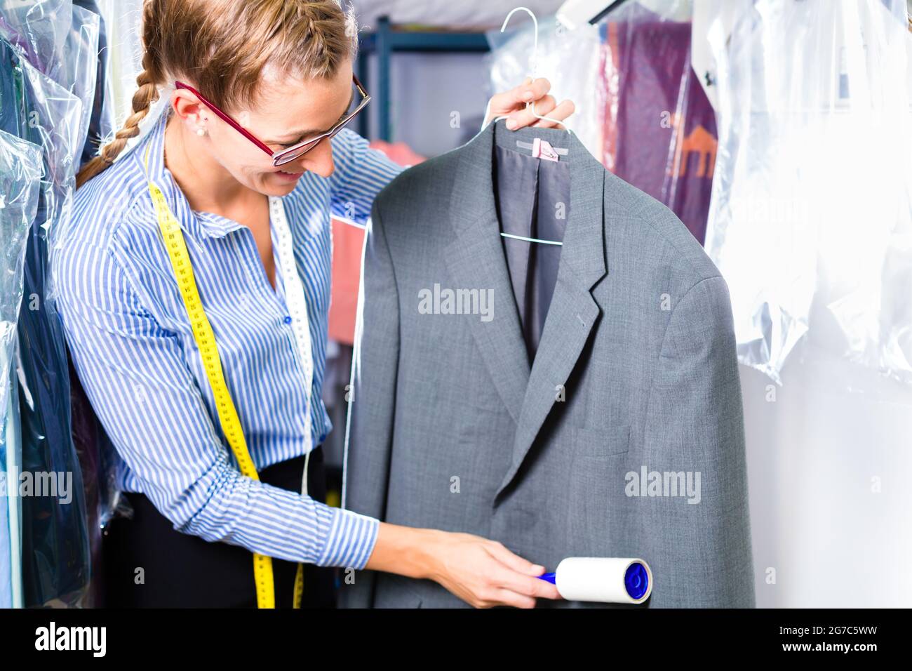 Female cleaner in laundry shop checking clean clothes removing lint with roller Stock Photo
