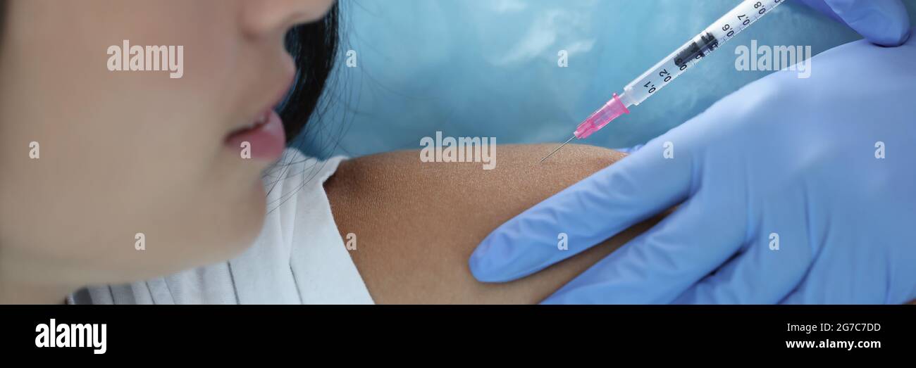 Doctor gives woman an injection in shoulder Stock Photo