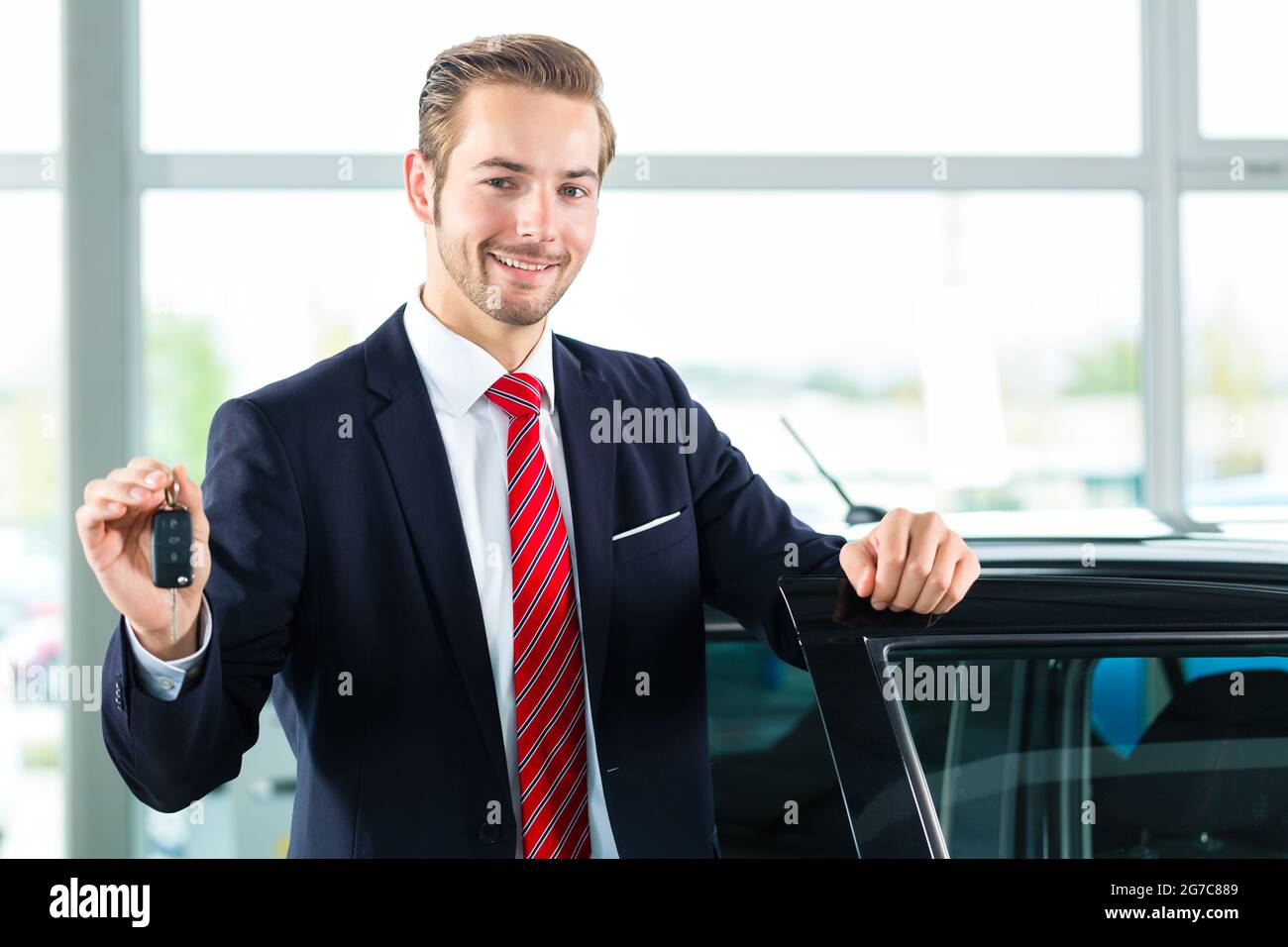 Seller or car salesman in car dealership with key presenting his new