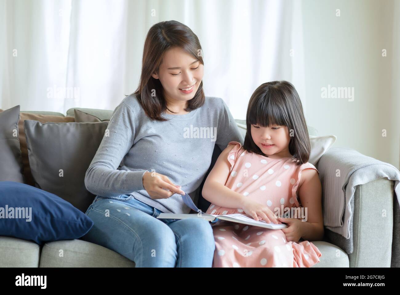 Happy asian mother teaching her cute kid daughter to studying in living room at home Stock Photo