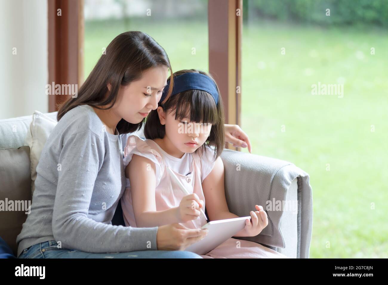 Happy asian mother teaching her cute kid daughter to studying in living room at home Stock Photo