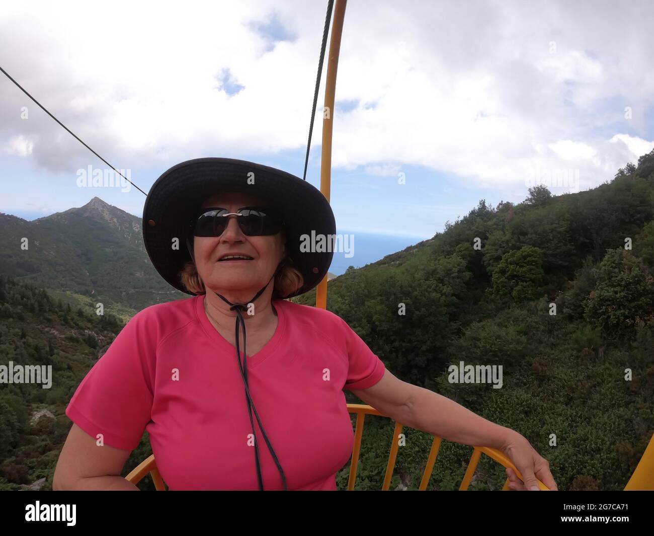 Senior woman enjoying cable car ride in yellow basket from the top of Elba island Stock Photo