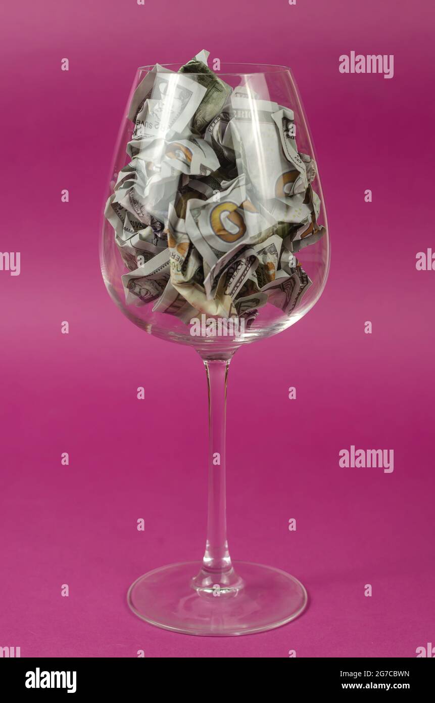 Wine glass full of paper money against  pink background. Crumpled hundred dollar bills in the glass. Stock Photo