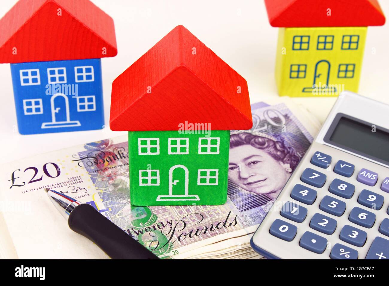 A house sitting on a pile of money, with a pen and calculator to symbolize house finance in the UK. Stock Photo