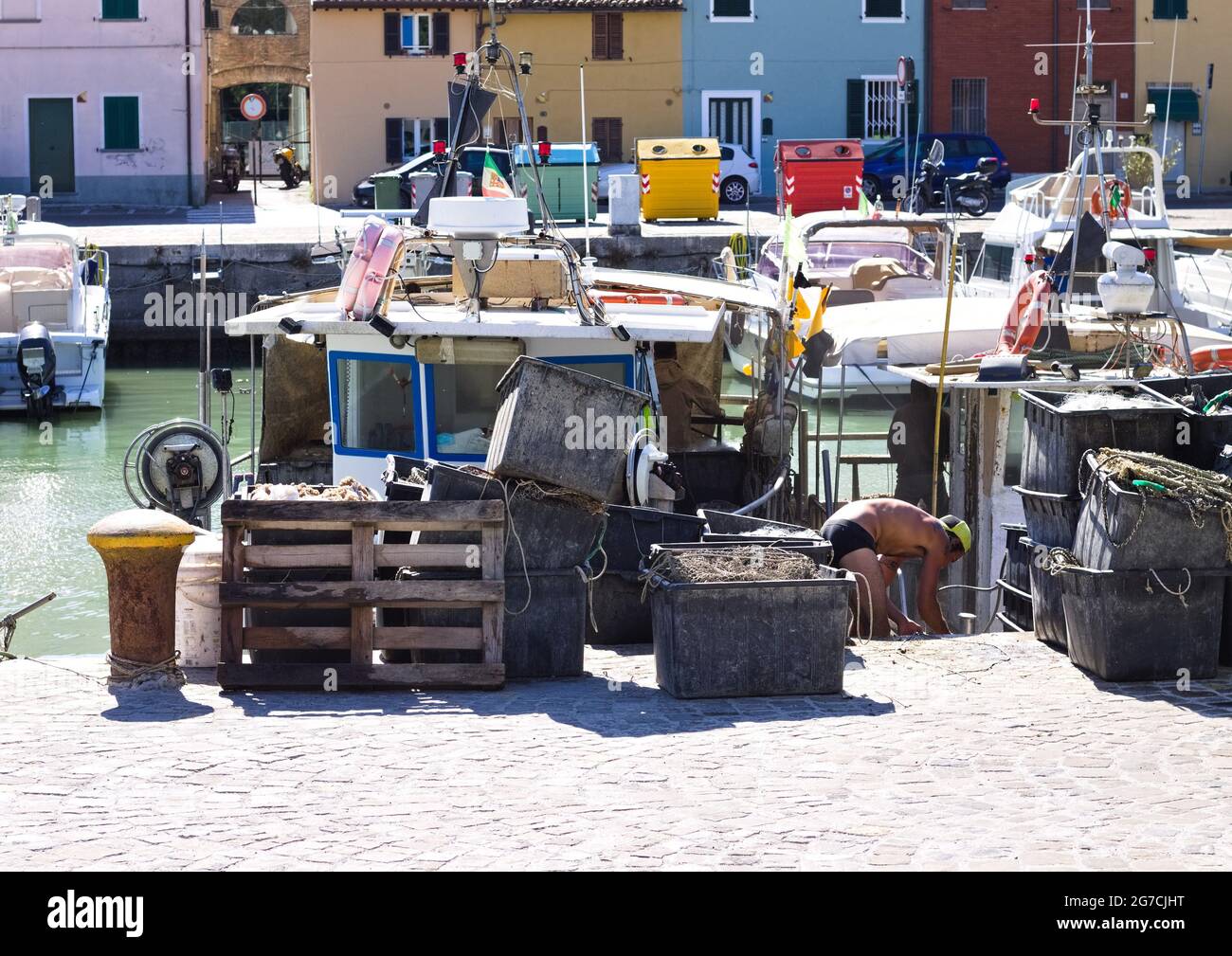 Pesaro, Italy - 09 july 2020: A fisherman is working on his fishing boat at the port of Pesaro with tools of the trade, fishing nets and boxes Stock Photo