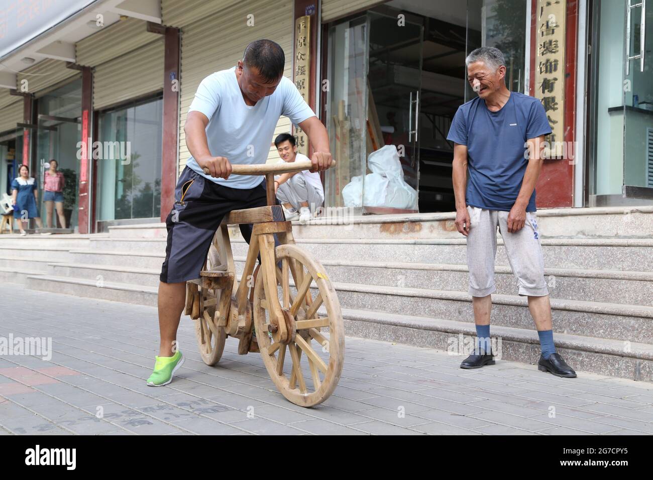 Pingliang, Pingliang, China. 13th July, 2021. On July 12, 2021, in Kongtong District, Pingliang City, Gansu Province, He Yong is demonstrating his pure wooden bicycle. He Yong, 58, from Kongtong District, Pingliang City, Gansu Province, became a household celebrity for his invention of the wooden bicycle. It took him more than a month from drawing pictures to finished products. He made wooden bicycles of more than 40 kilograms from waste walnut wood. The bicycles did not use a single nail, and were all linked by wood. You can watch and ride. According to He Yong, he rode home from Ko Stock Photo
