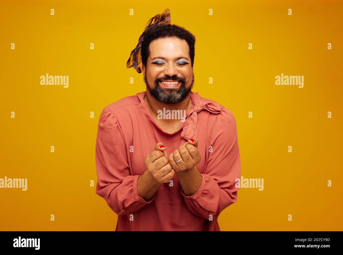 Happy bearded man in female outfit and makeup. Drag queen feeling excited on yellow background. Stock Photo