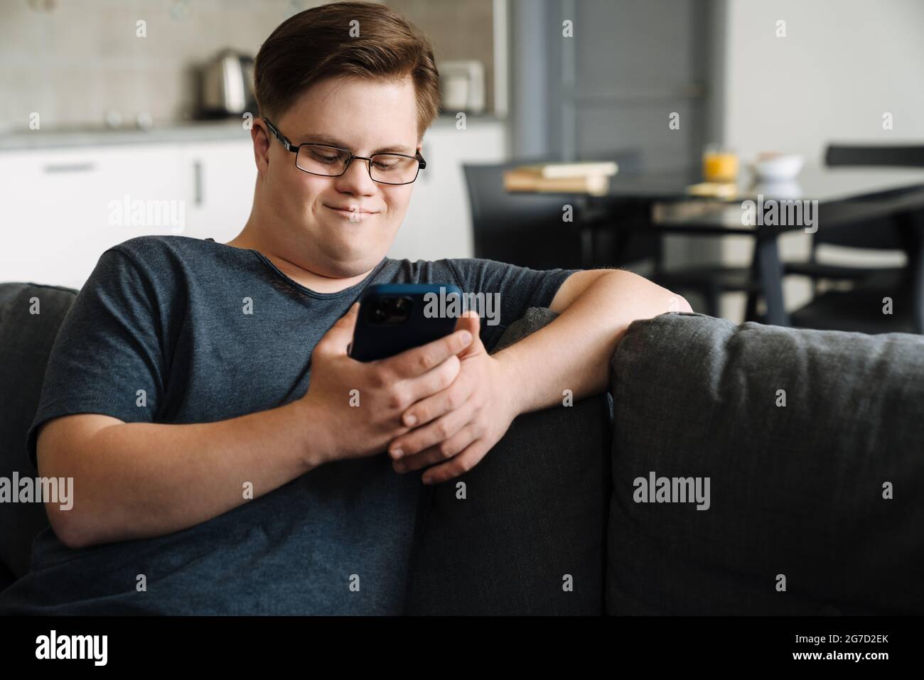Young man with down syndrome using cellphone while sitting on couch at home Stock Photo