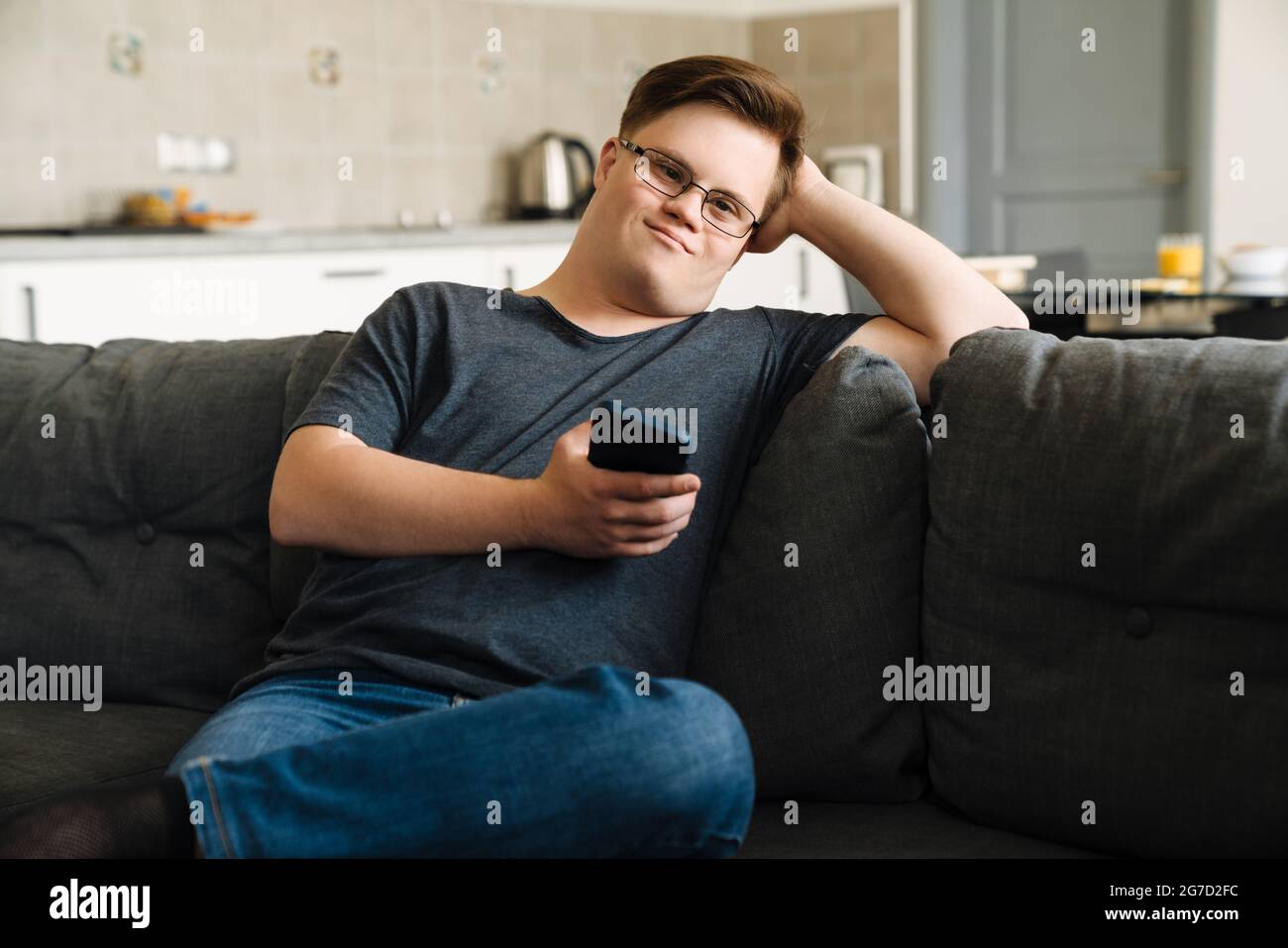 Young man with down syndrome using cellphone while sitting on couch at home Stock Photo