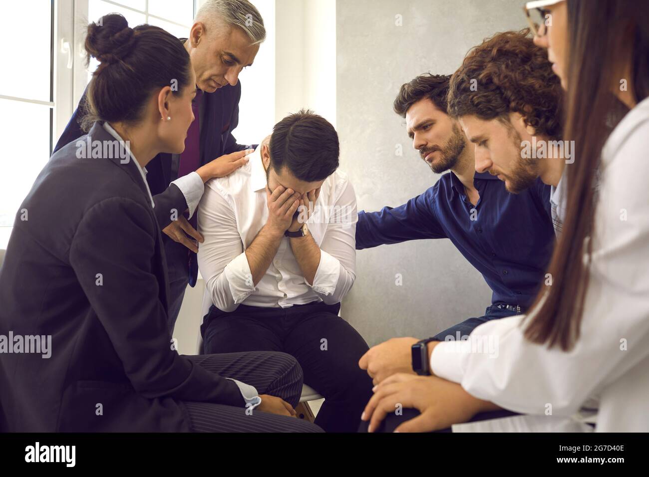 Compassionate people in group therapy comforting and supporting distraught young man Stock Photo
