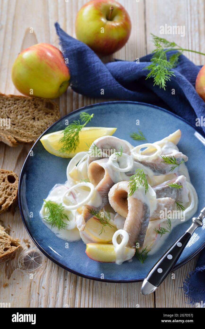 Salty herring fillets with apple slices, onion rings and yoghurt cream sauce Stock Photo