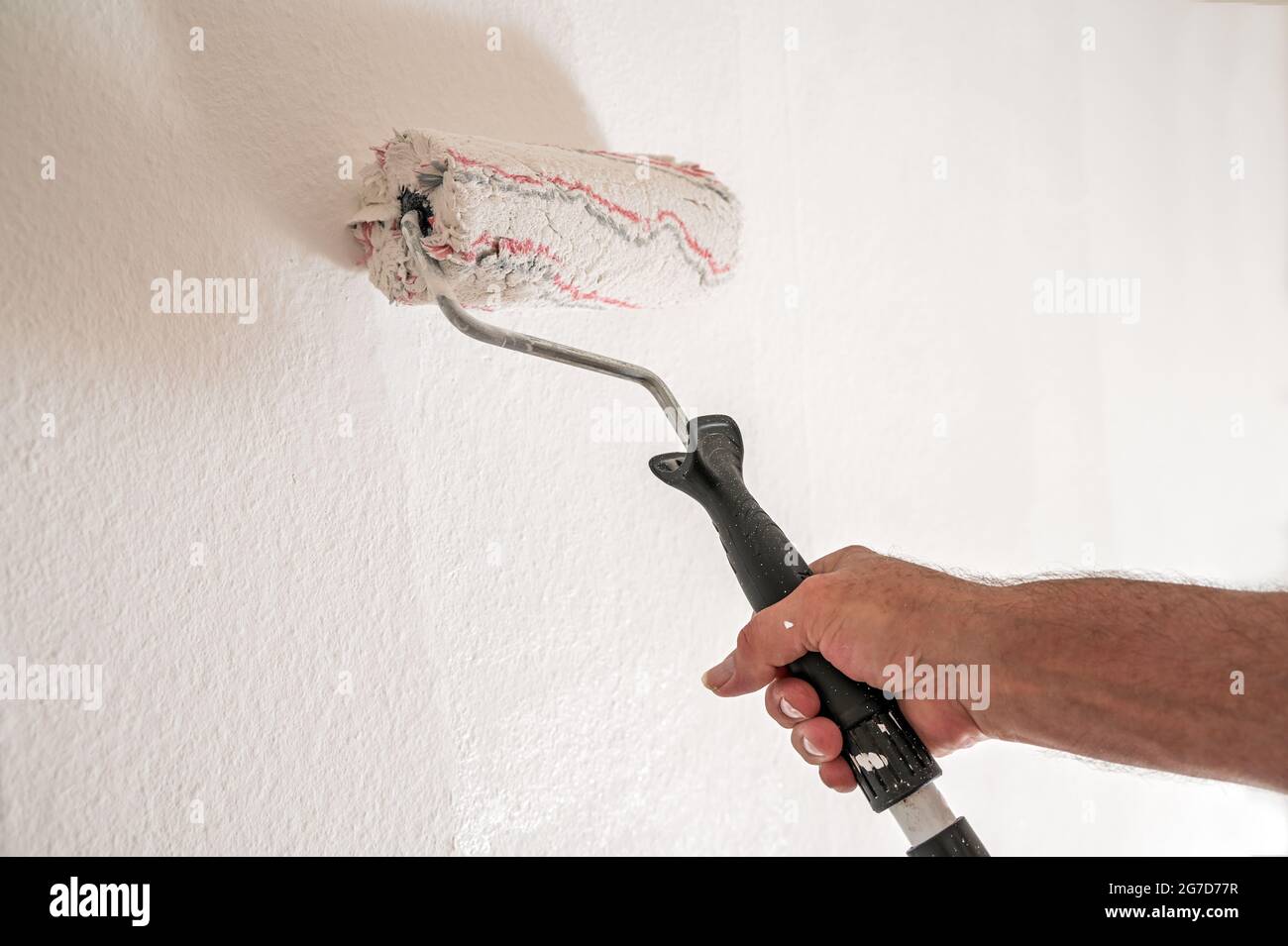 Male hand with paint roller painting the walls, renovation concept when moving to a new apartment, real estate concept, copy space, selected focus, na Stock Photo