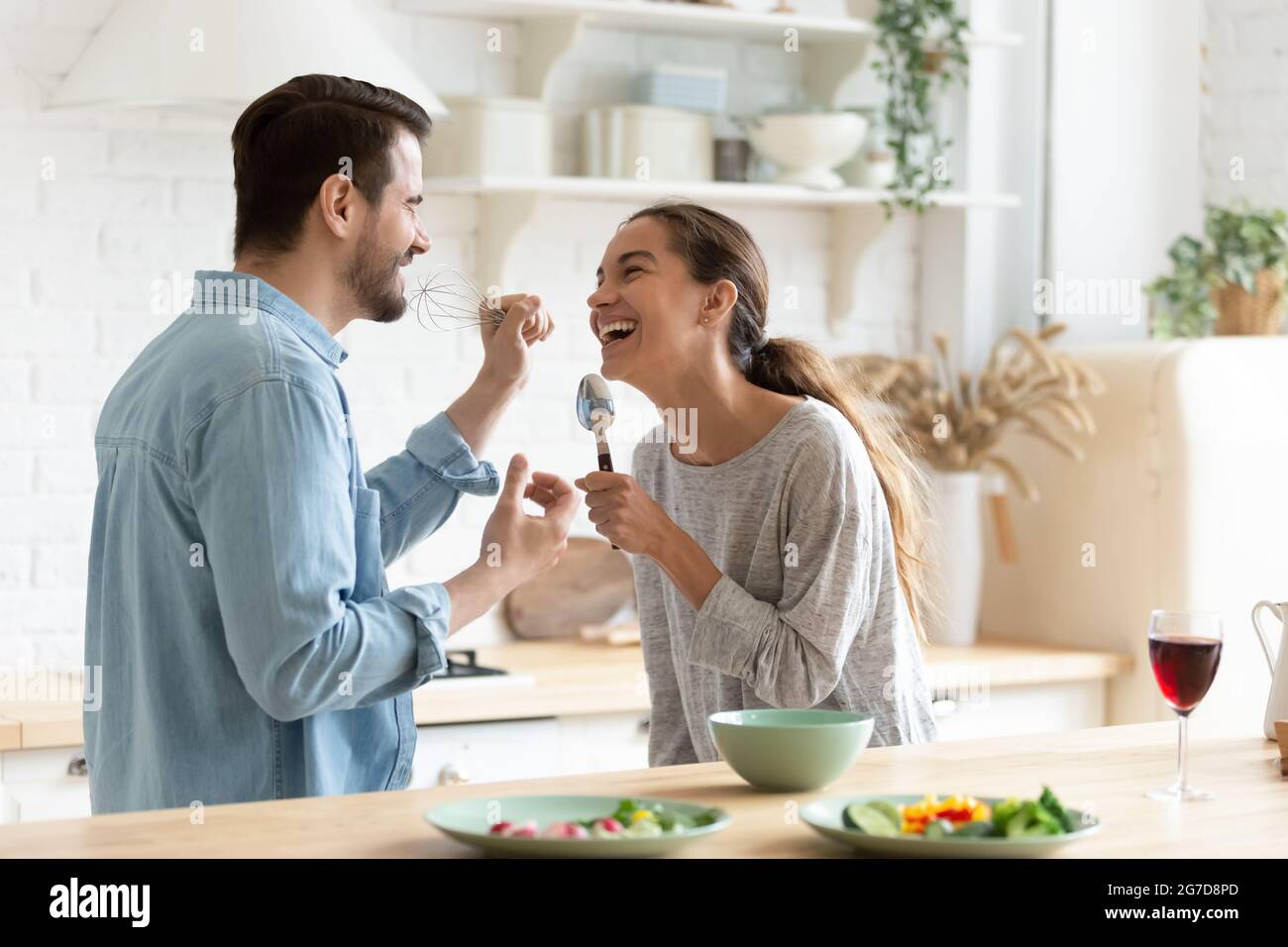 Cheery couple holding kitchenware singing having fun together in kitchen Stock Photo