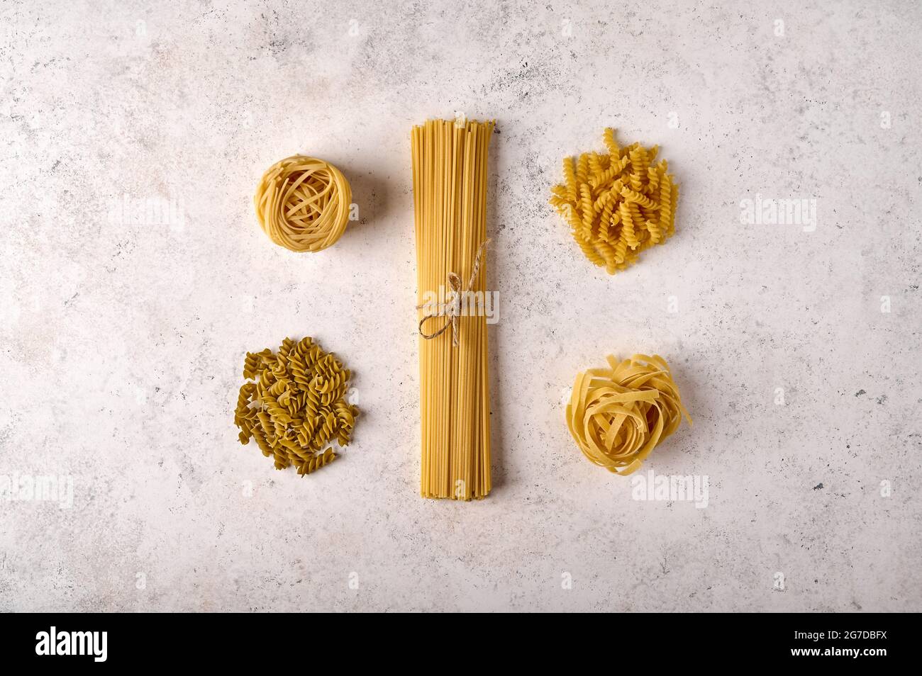 Uncooked raw bunch of spaghetti, fettuccine, girandole and tagliatelle on grey textured background. Copy space. Top view Stock Photo