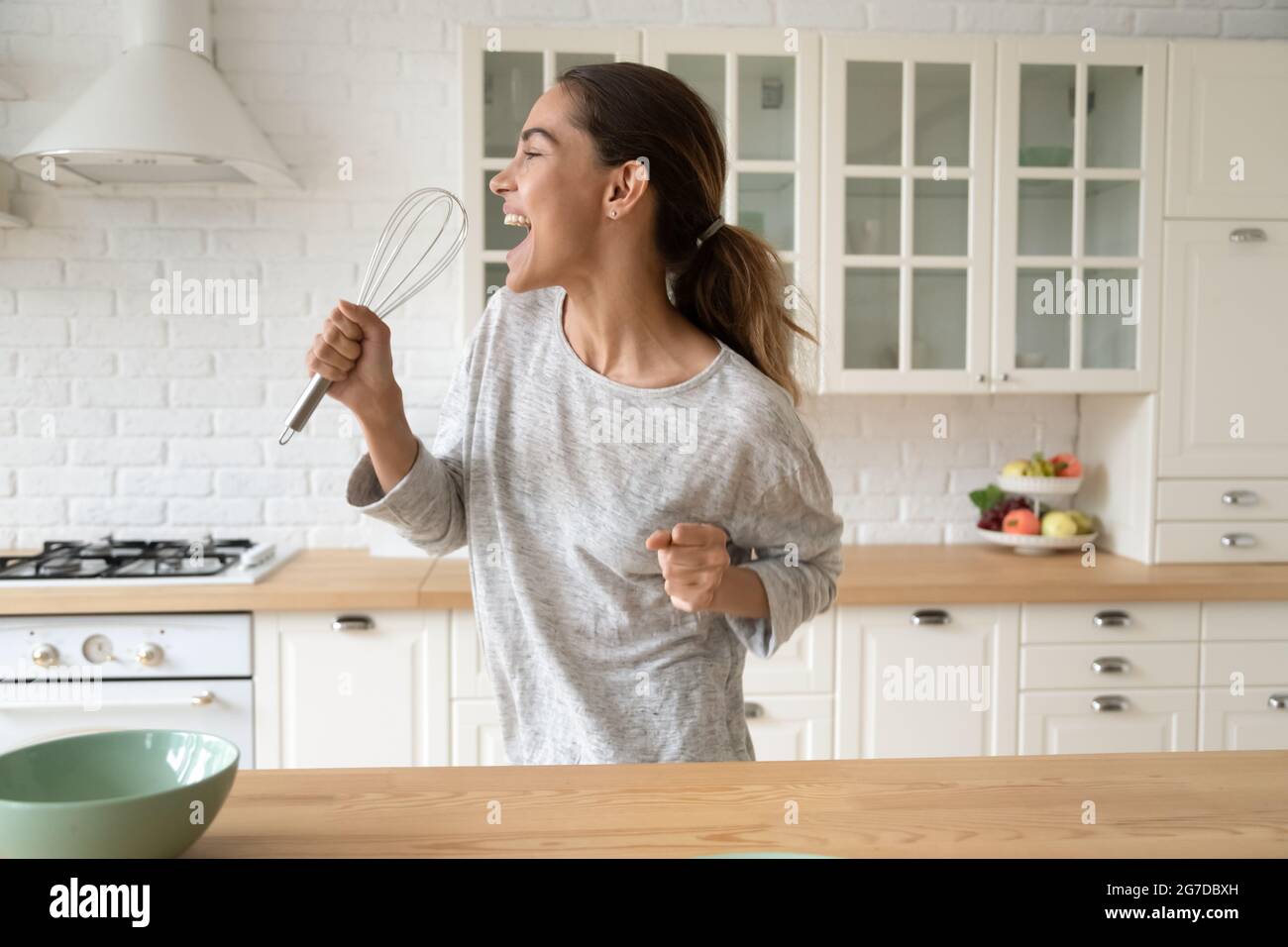 Female holding whisk opens mouth singing song standing in kitchen Stock