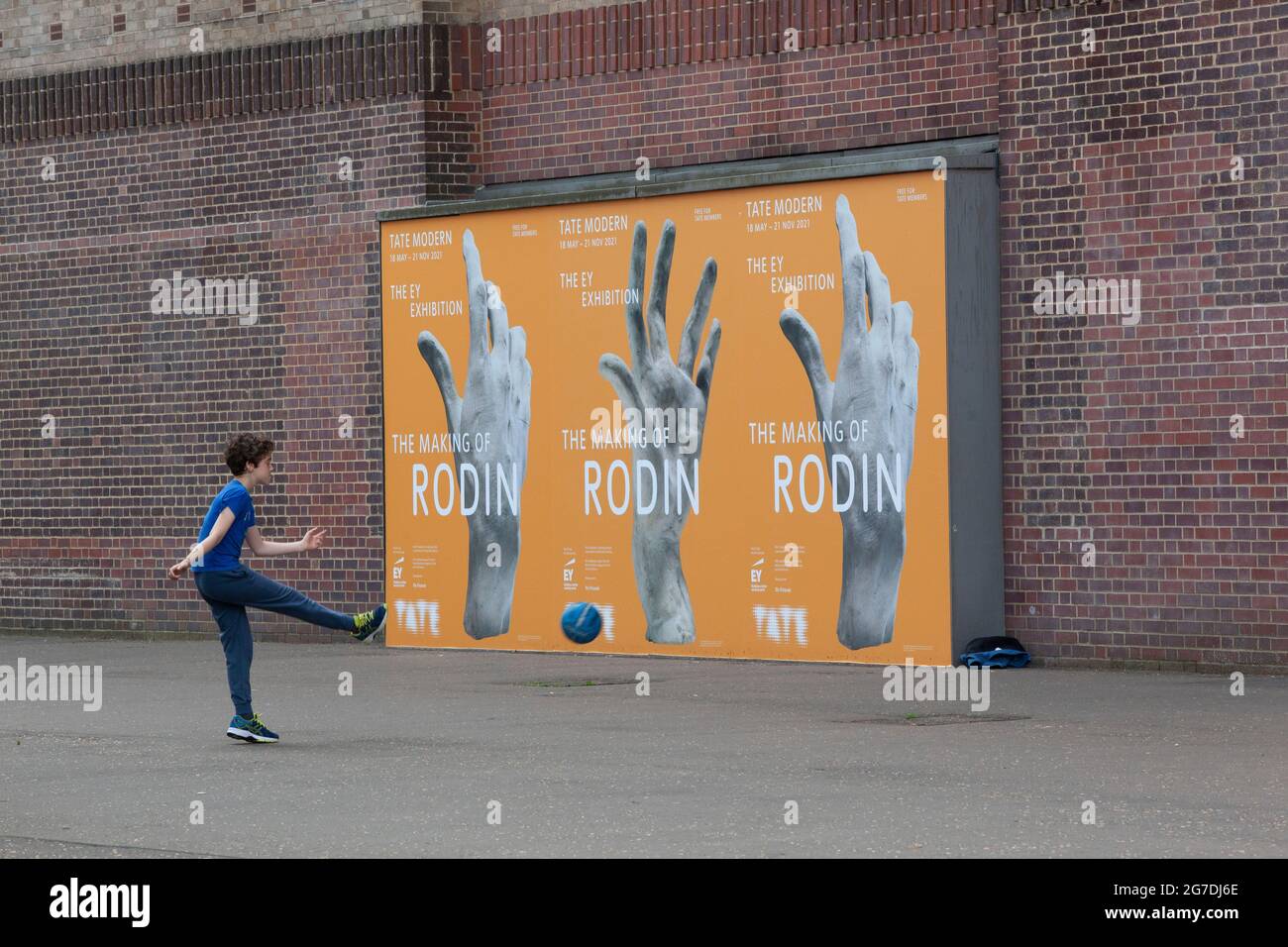London, UK, 13 July 2021: A boy kicks a ball against a wall at Tate Modern, nect to posters for an exhibition of Rodin's sculptures. Places for outdoor play have been reduced over the years and not all children have access to play space. Anna Watson/Alamy. Stock Photo