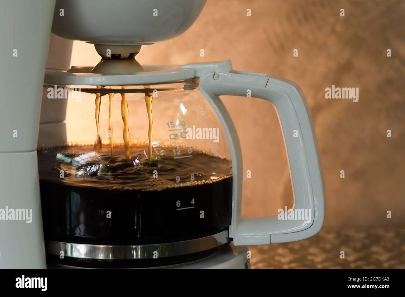Coffee drip pot on process with coffee drip inside. Blurry gray concrete background with warm