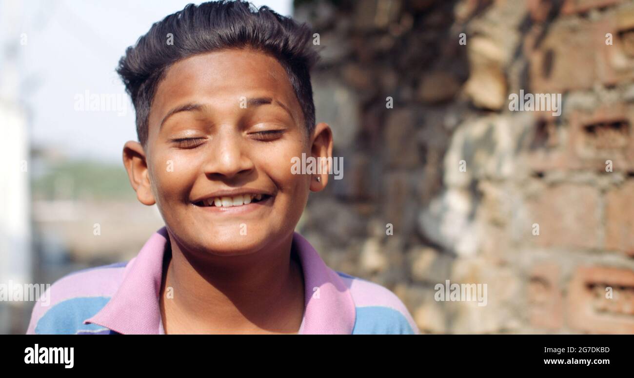 Closeup of a young Indian boy grinning at the camera with his eyes closed on a blurry background Stock Photo