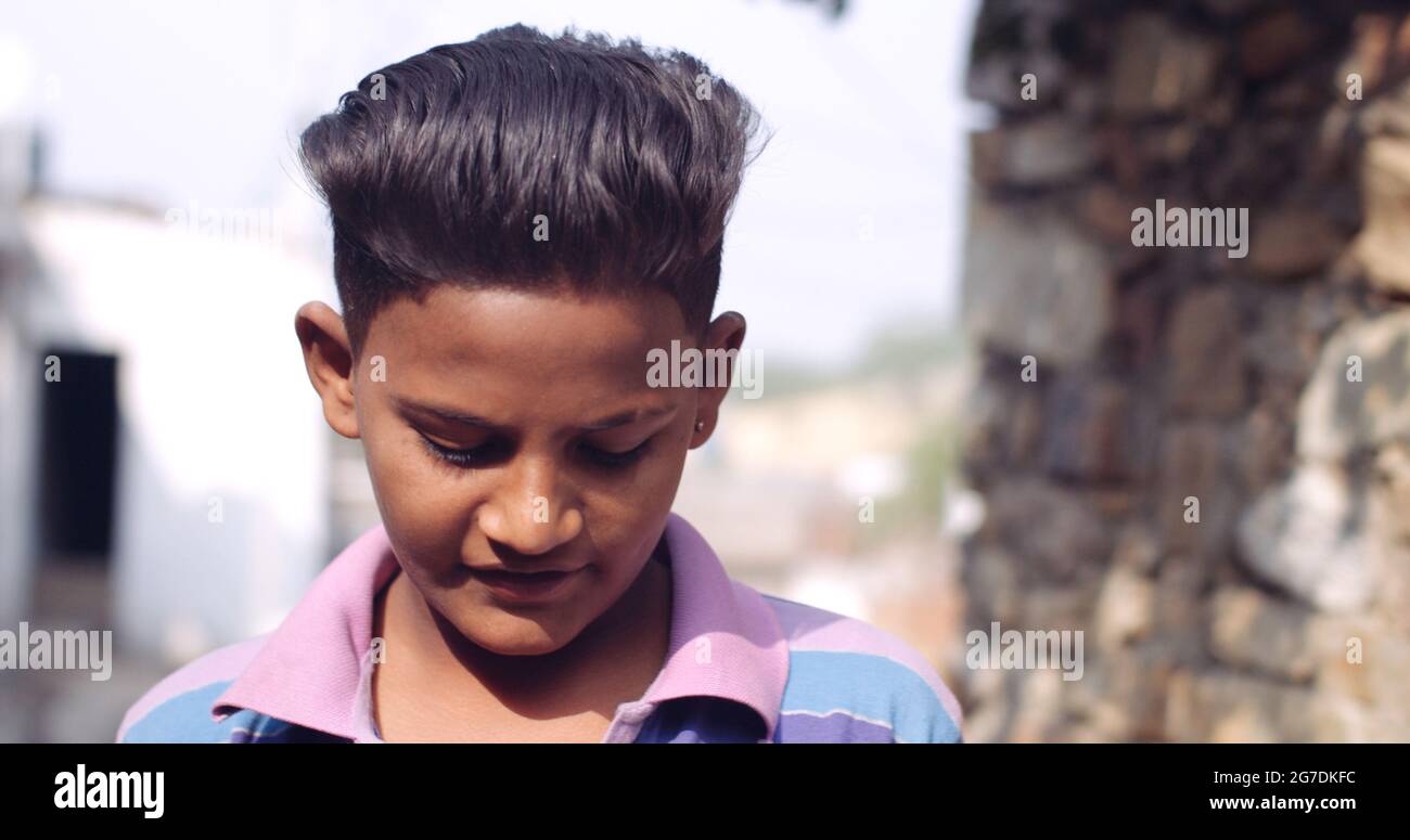 Closeup of a young South Asian boy looking down while wearing a colorful striped shirt Stock Photo
