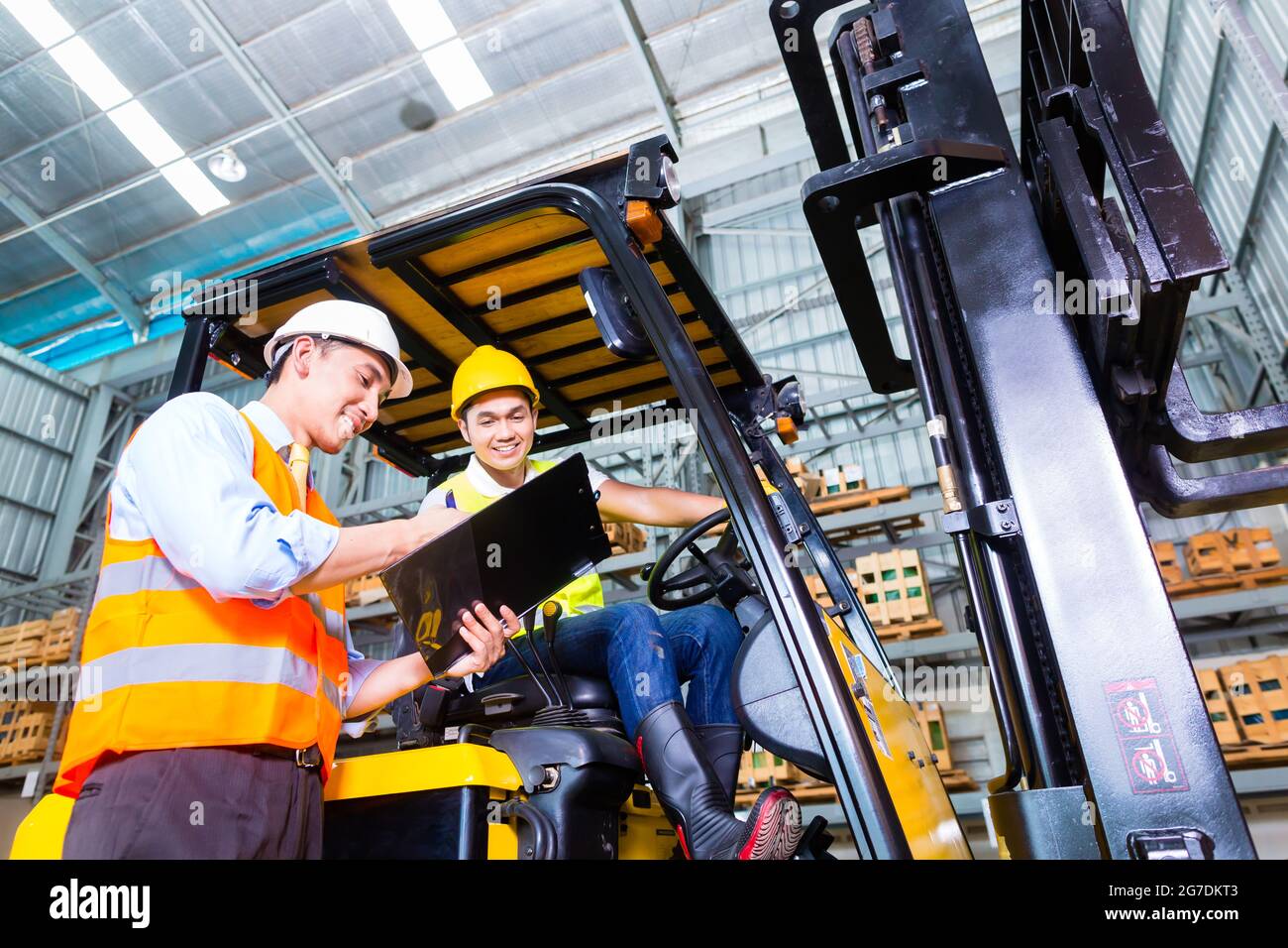 Asian fork lift truck driver discussing checklist with foreman in warehouse Stock Photo