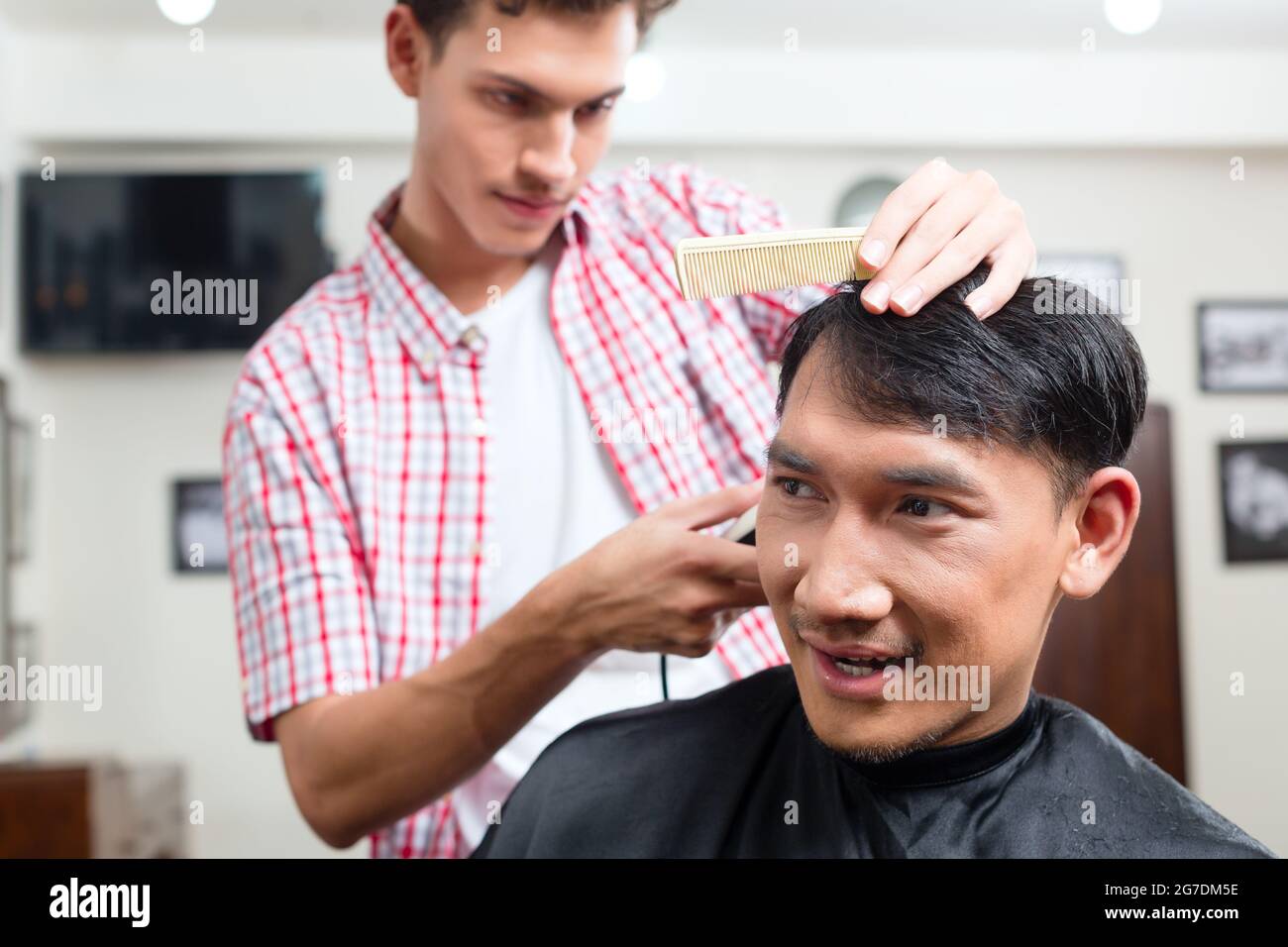 Barber making haircut of an attractive man in barbershop Stock Photo