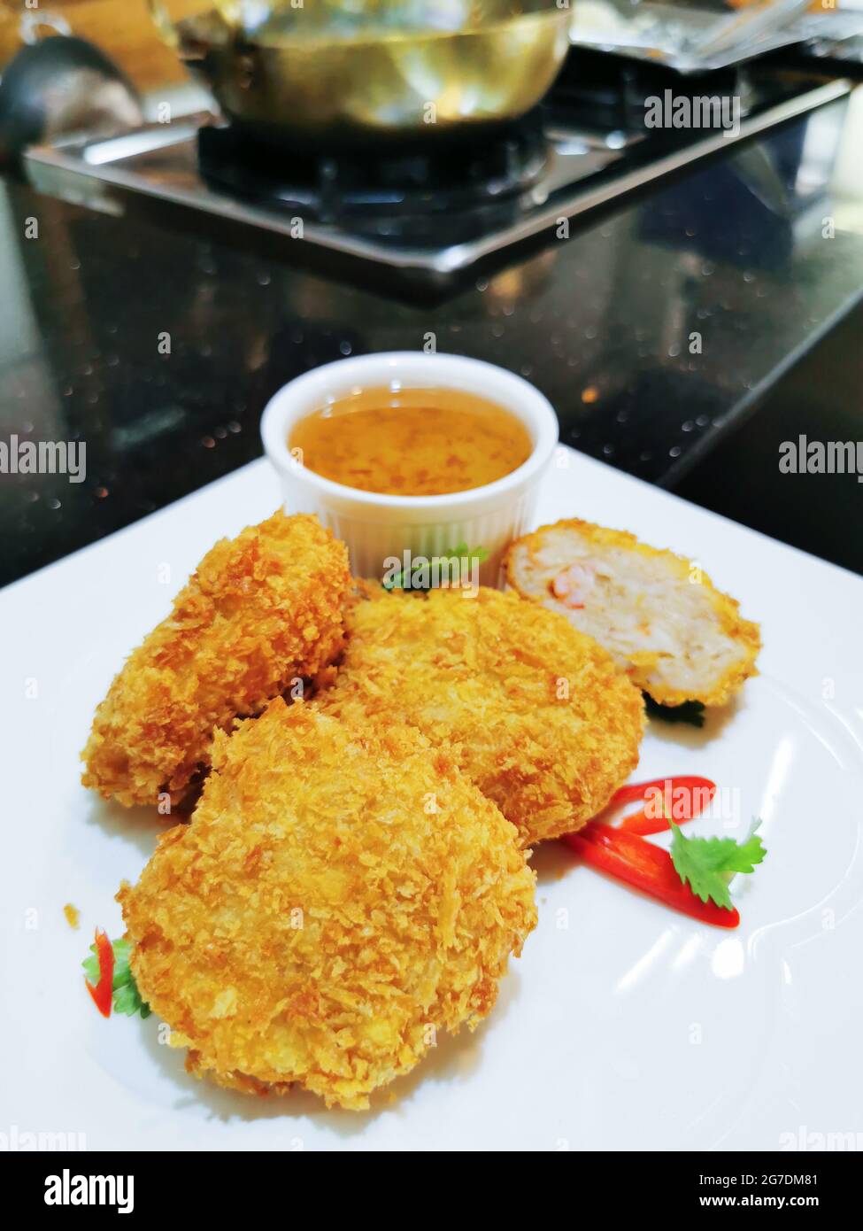 Deep fried prawn cake served on white ceramic plate with sweet and sour dipping sauce on small bowl on the plate, garnish with sliced red chili pepper Stock Photo