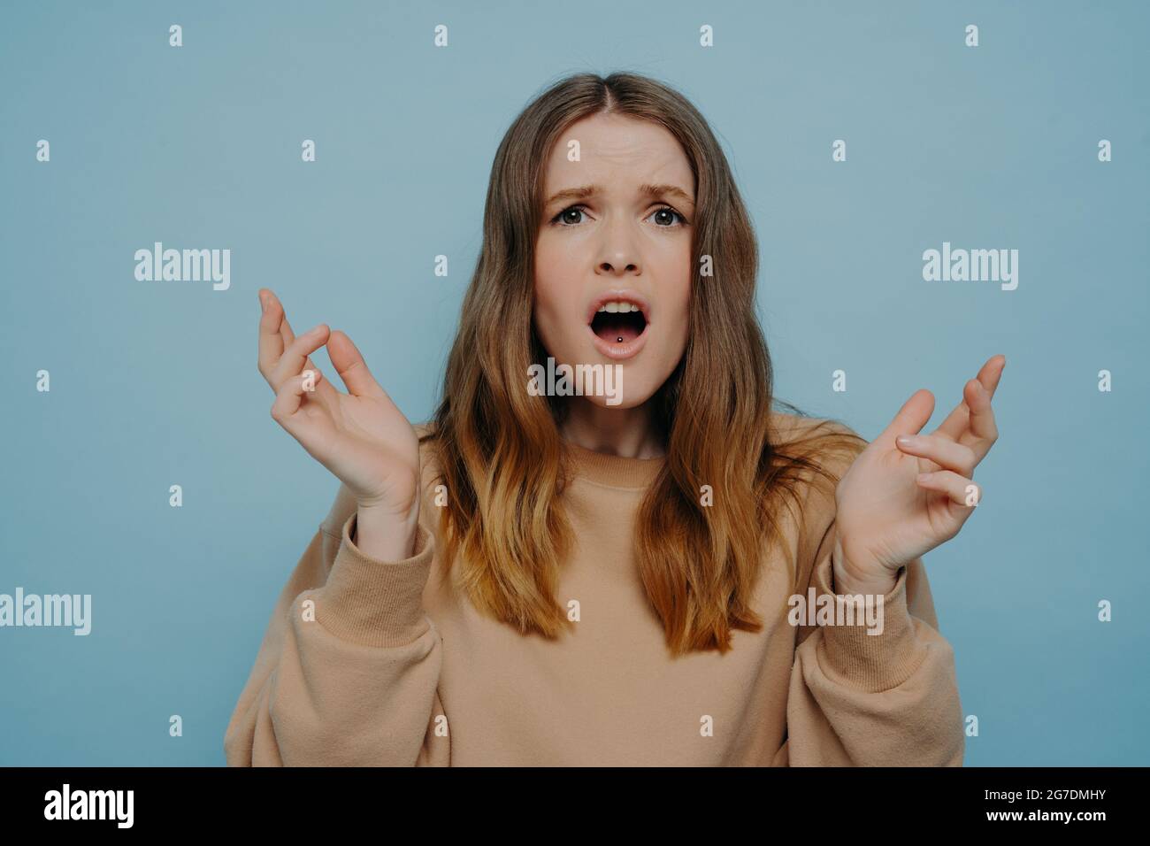 Cute teenage girl expressing disbelief and shock standing against blue studio wall Stock Photo