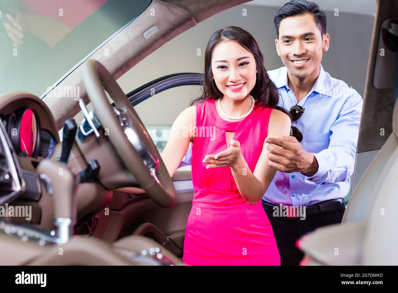 Asian couple choosing luxury car in auto dealership looking at the interior Stock Photo