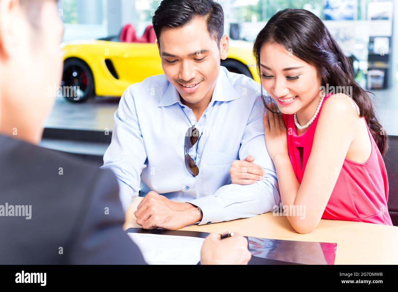 Asian Couple signing sales contract for car at dealership Stock Photo