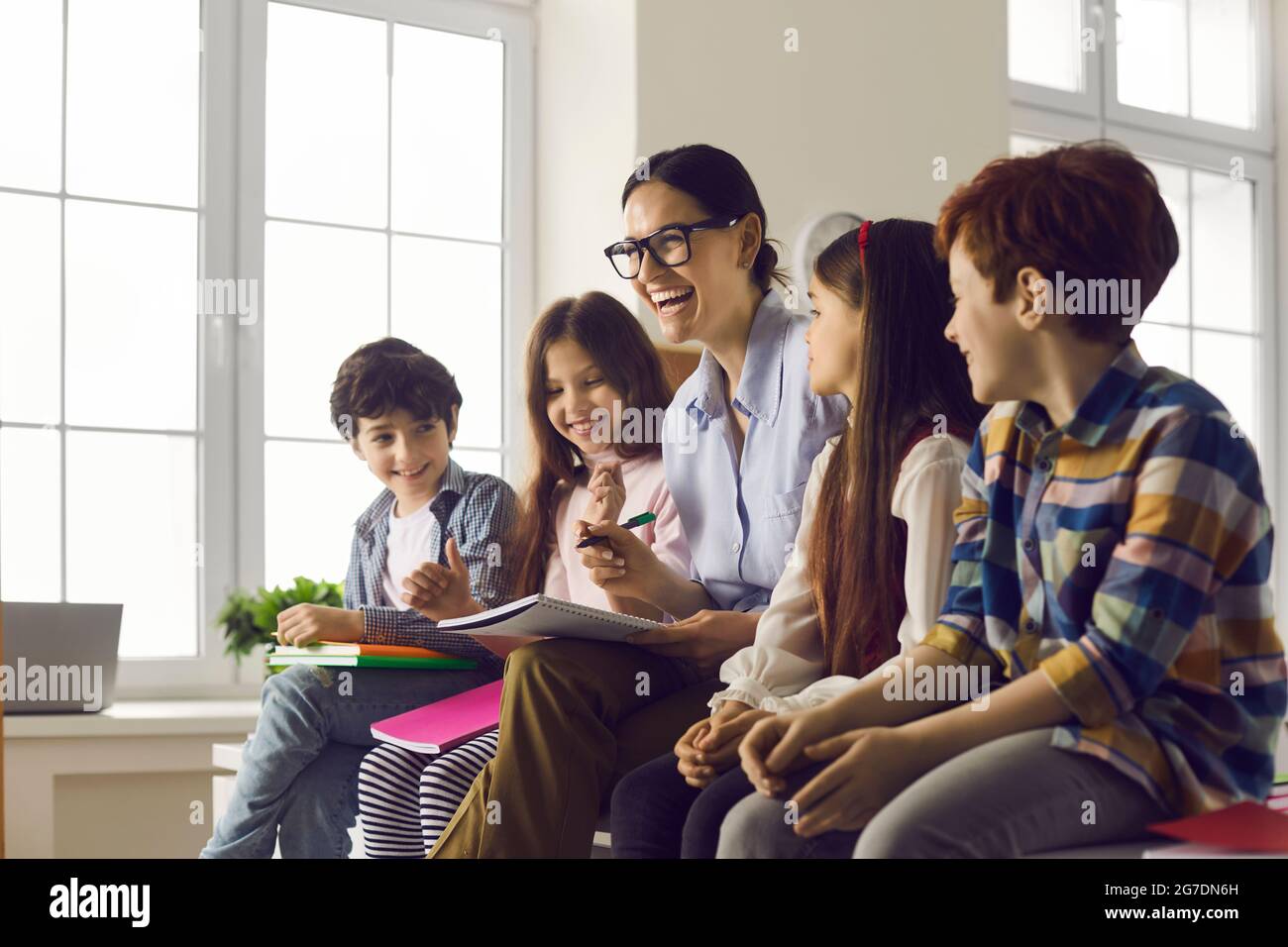 Teacher and pupils laughing while checking task in copy-book in classroom Stock Photo